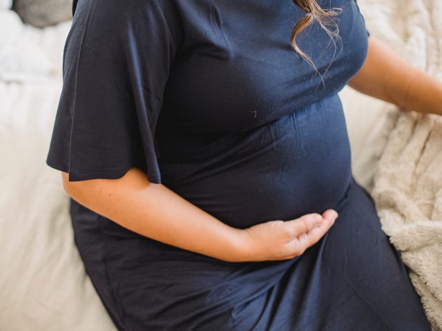 kobieta w ciąży w granatowej sukience siedzi na brzegu łóżka