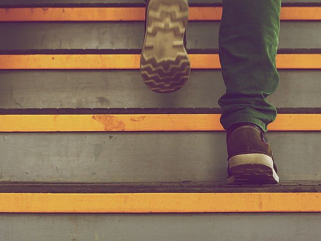 Widok na buty osoby wbiegającej po schodach. Poszczególne schodki mają żółte pasy na krawędziach