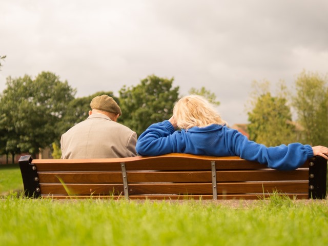 dwoje seniorów tyłem do obiektywu siedzi na ławce w parku