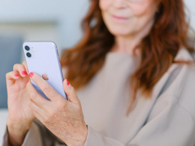 starsza kobieta trzyma w ręku smartfona i patrzy w niego
