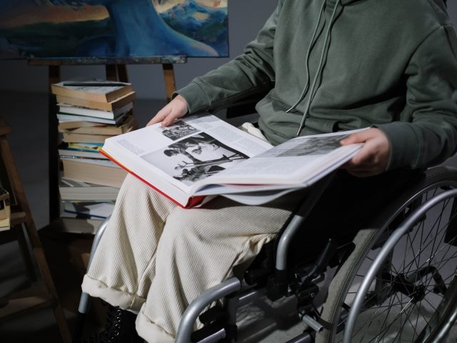 chłopak na wózku trzyma na kolanach dużą książkę w tle obraz i książki