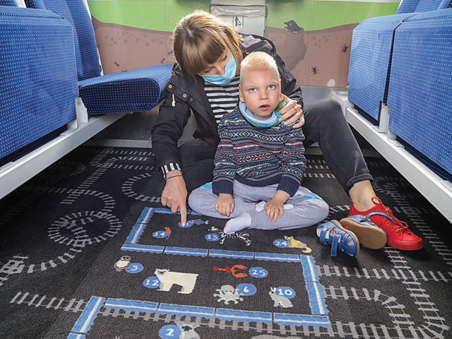 kobieta z dzieckiem z niepełnosprawnością siedzi na dywanie w wagonie Combo, pokazuje synowi grę na dywanie