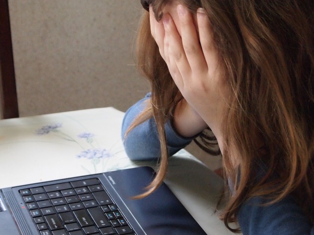 dziewczynka ukrywa twarz w dłoniach, siedzi przed laptopem