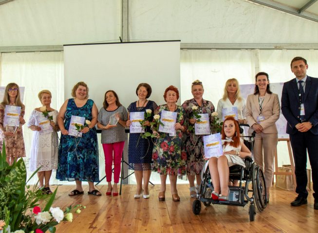 10 kobiet w rzędzie stoi na scenie pozując do zdjęcia laureatki z dyplomami z brzegu jeden mężczyzna