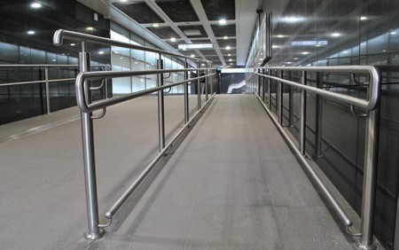 Podziemny korytarz. Po prawej pochylnia dla osób z niepełnosprawnością z poręczami na dwóch wysokościach