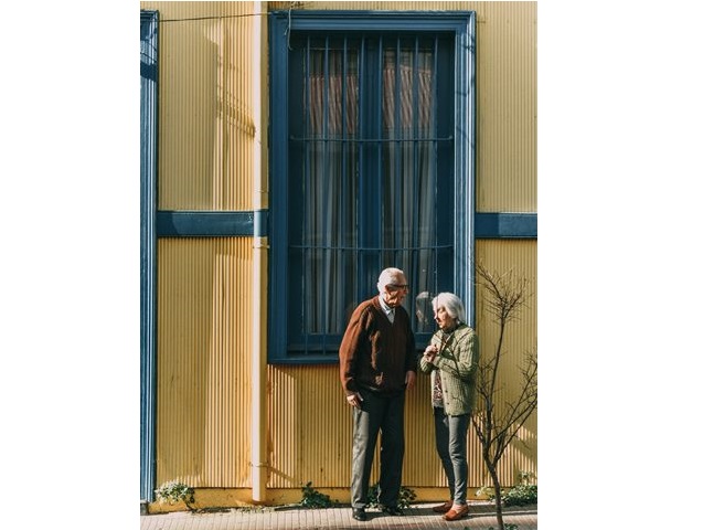 kobieta i mężczyzna stoją i rozmawiają na chodniku przy budynku za nimi okno z kratami