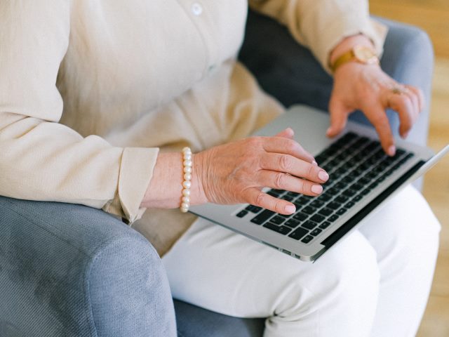 seniorka siedzi na fotelu i pisze na laptopie