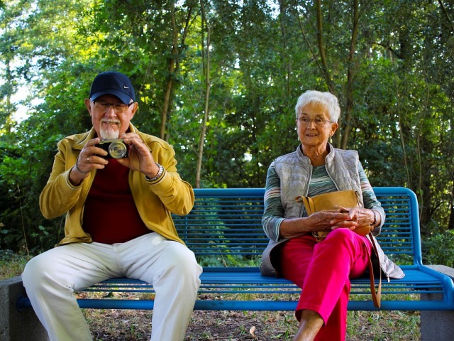 starszy mężczyzna i kobieta uśmiechnięci siedzą na ławce