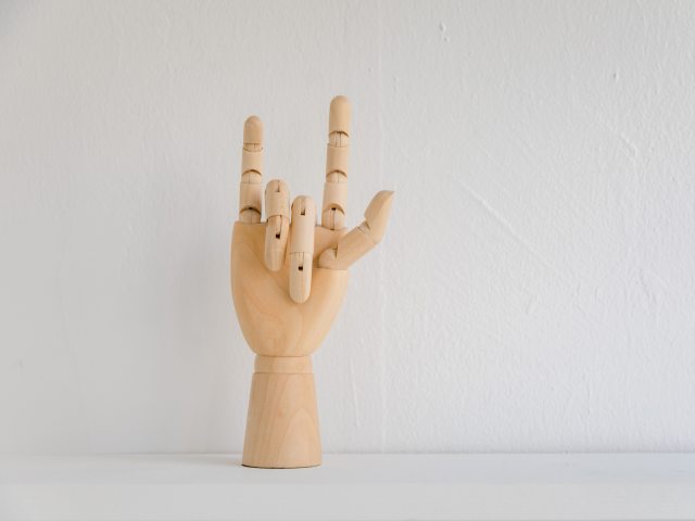 Drewniana dłoń wykonująca gest w języku migowym.