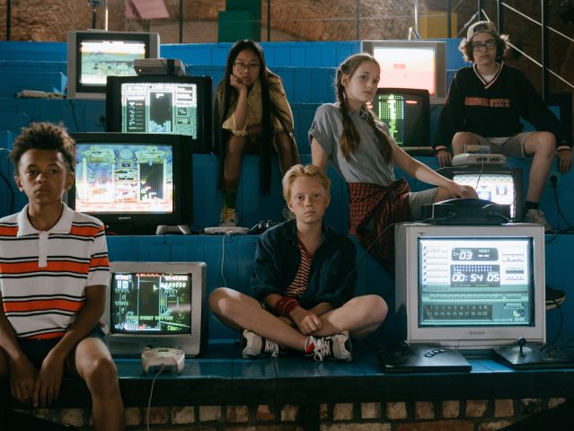 grupa nastolatków siedzi na ławkach pomiędzy ekranami komputerów