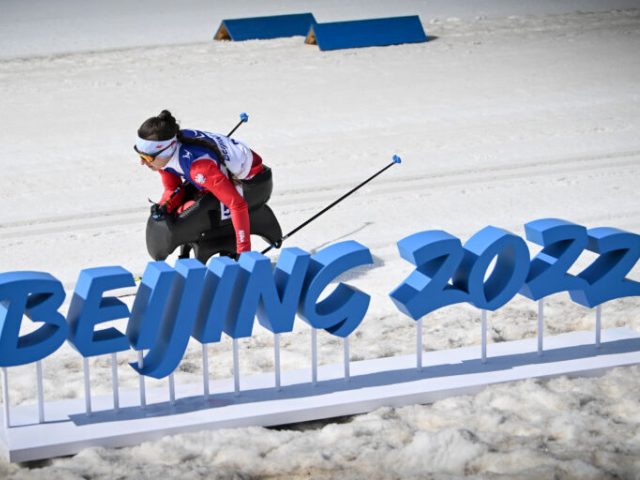 Polska zawodniczka jedzie na monoski, mija napis Beijing 2022