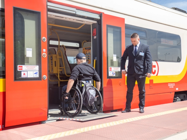 Pociąg i asystent pomagający osobie na wózku wjechać do pociągu.