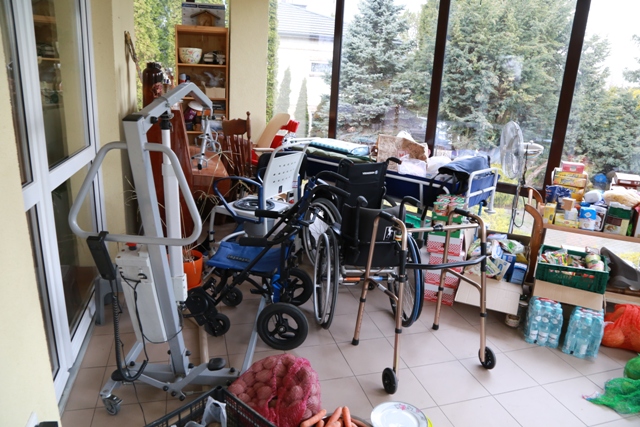 Pomieszczenie loggia, jest dużo sprzetu dla osób z niepełnosprawnościami, balkoniki, wózki, ale też kartonów z jedzeniem, wody