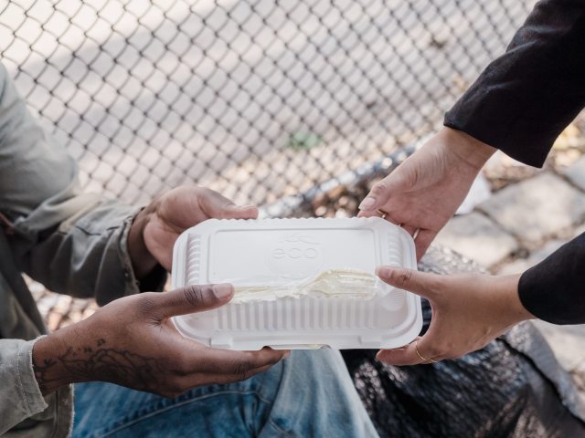 Na zdjęciu przedstawione są dłonie osoby bezdomnej i tej, która wręcza mu jedzenie