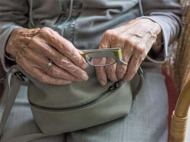 zbliżenie na ręce starszej kobiety, która chowa do torebki okulary 
