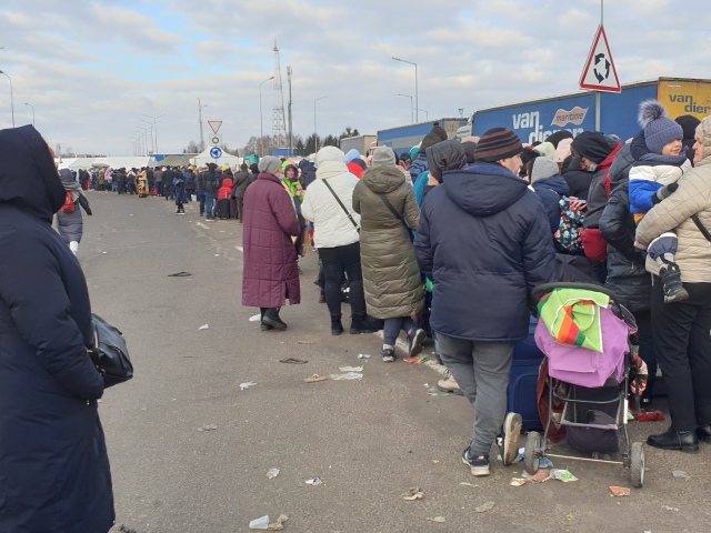 Bardzo długa kolejka tłumu ukraińskich uchodźców stoi na drodze asfaltowej wśród tirów