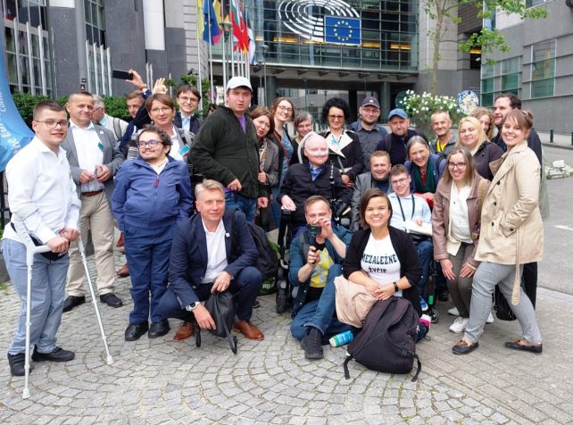 grupka osób z niepełnosprawnościami i opiekunów pod Parlamentem Europejskim w Brukseli