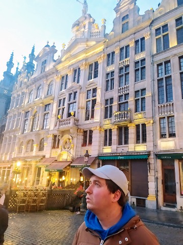 młody mężczyzna w czapce z daszkiem, w tle zabytkowa kamienica w Brukseli