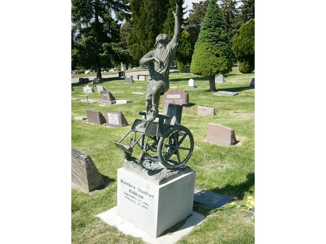 Rzeźba nagrobkowa przedstawiająca chłopca stojącego na wózku, który sięga do nieba.