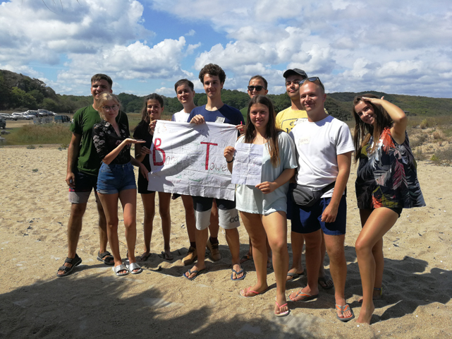 grupa młodych osób, uśmiechniętych pozuje do zdjęcia na plaży