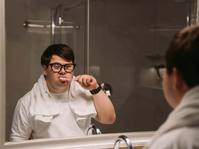 Mężczyzna z Zespołem Downa myje zęby przed lustrem.