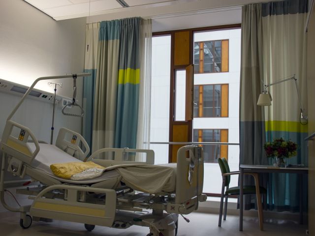 szpitalna sala, w którym stoi puste łóżko dla chorego, w rogu stolik z krzesłem i bukietem