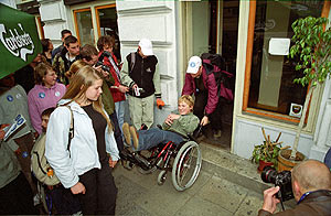 mężczyzna pomaga wyjechać kobiecie na wózku ze sklepu, przed którym jest schodek