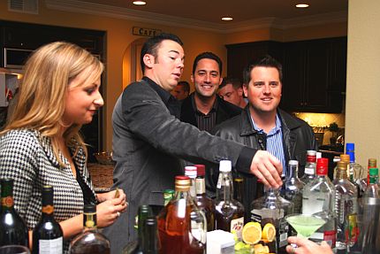 Kobieta i trzech meżczyzn stoją przy stole z butelkami alkoholu