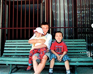 rodzic przytula małe dziecko siedząc na ławce, obok drugie dziecko