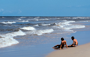 dwie osoby leżące na linii fal morskich a plaży