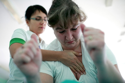 Rehabilitantka przytrzumuje za klatkę piersiową pacjentkę podczas ćwiczeń
