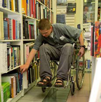 Student z niepełnosprawnością przy półce z książkami